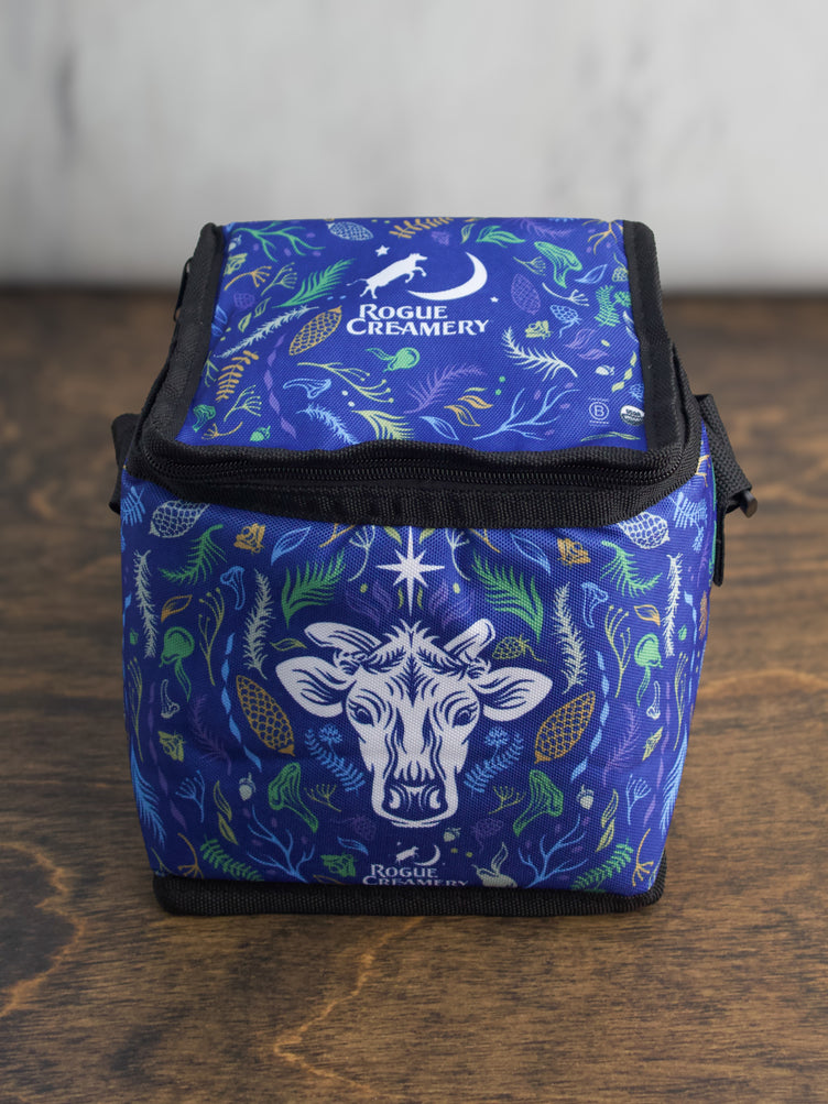A compact blue insulated cooler bag with a cow’s head and floral design on the front, Rogue Creamery logo above.
